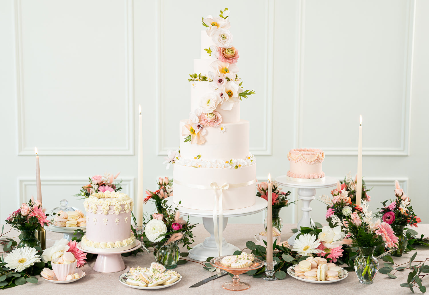 Table featuring cakes cookies and macarons in pink and peach garden floral theme with greenery