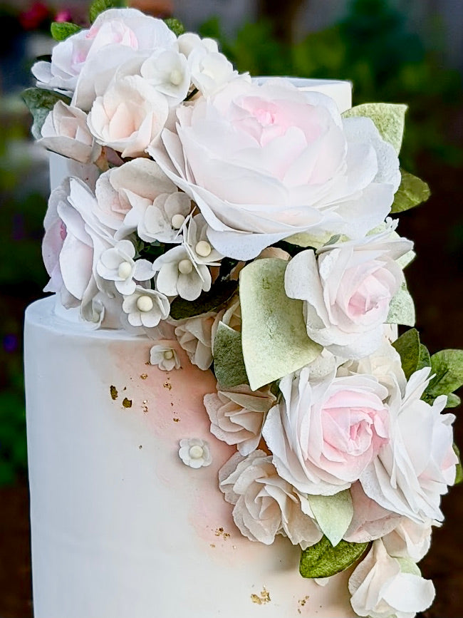 wafer paper flowers on wedding cake in shades of pink, blush, cream, and green with gold leaf accents